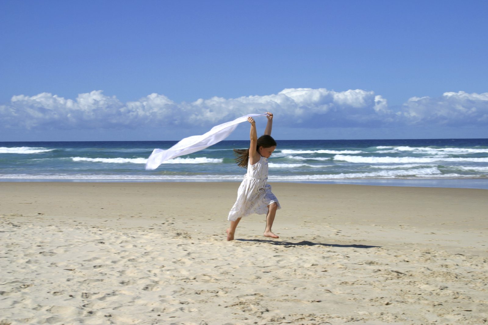A child running on a beach, holding a white scarf in the wind