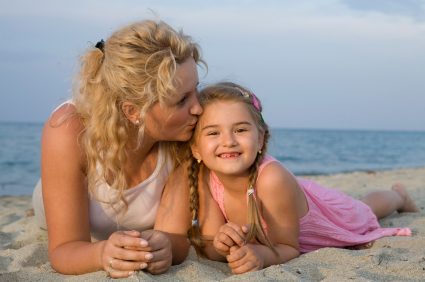 A mother kissing her smiling daughter on the head at the beach